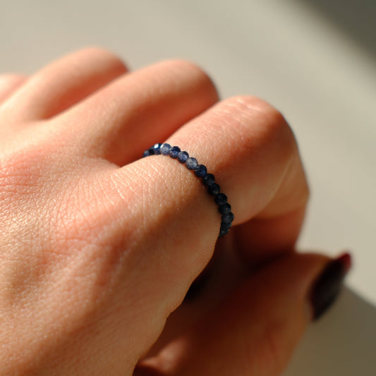 Close-up of a hand wearing a dark blue beaded ring on a neutral background