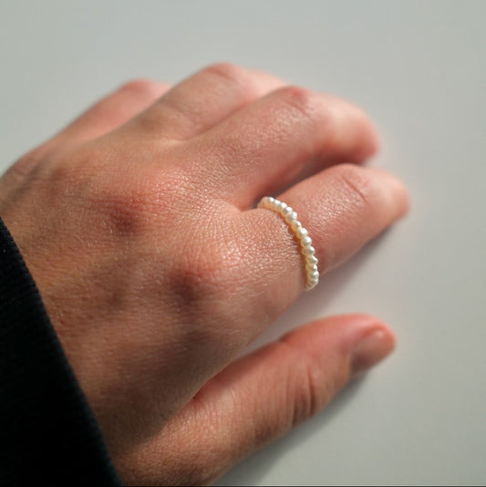 Hand wearing a pearl ring on a neutral background
