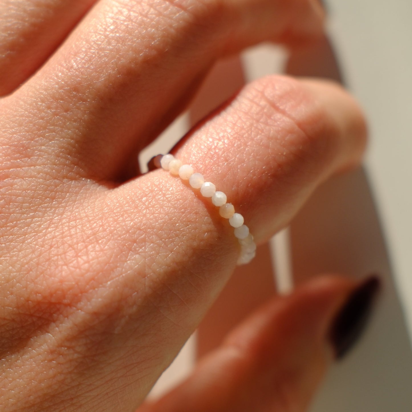 Close-up of a hand wearing a delicate pearl bracelet against a neutral background