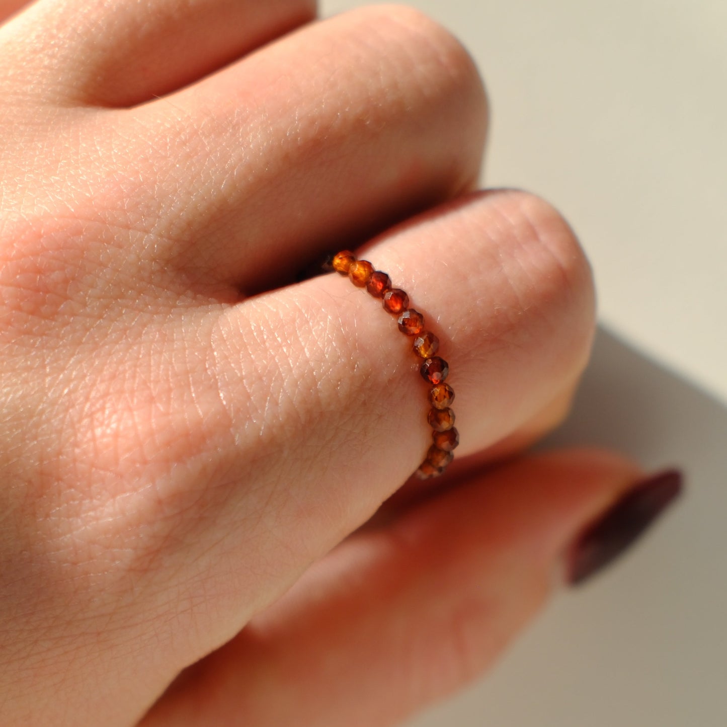 Hand wearing a red beaded ring on a neutral background