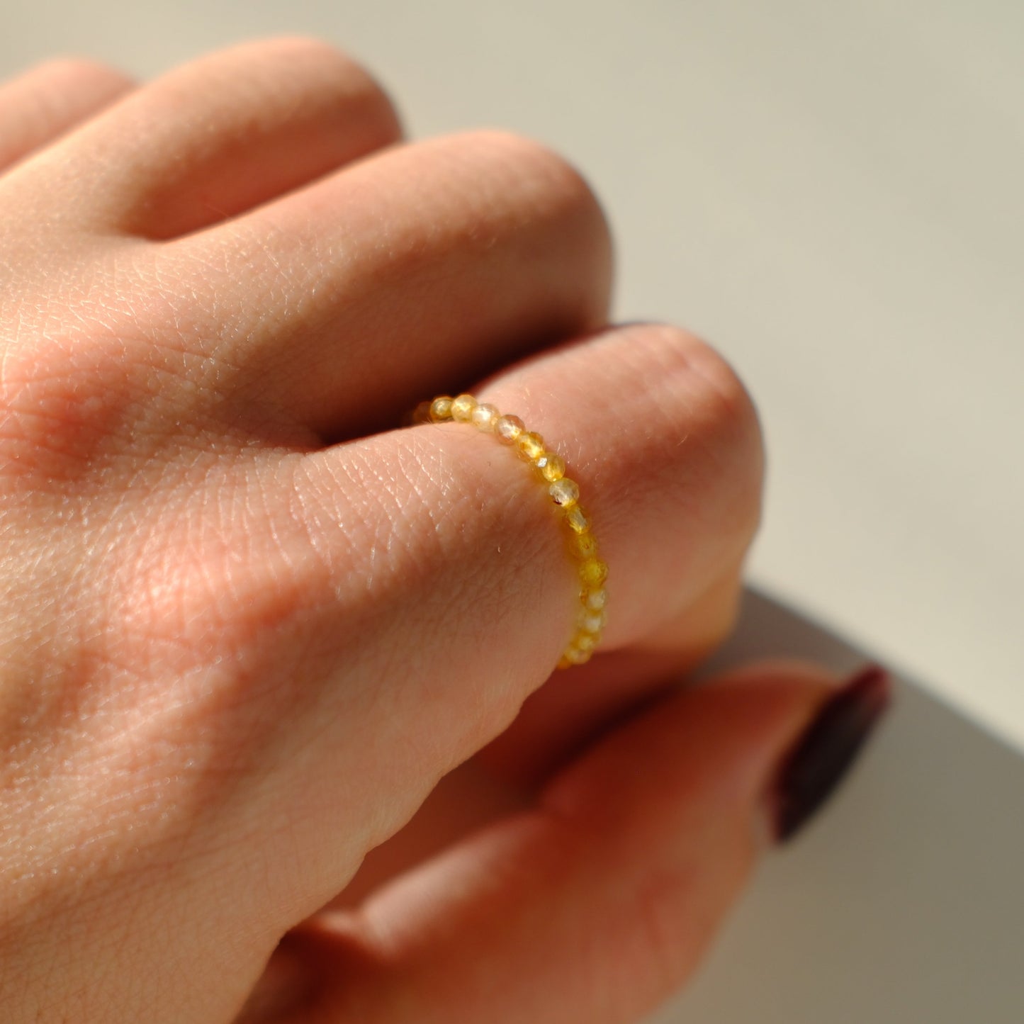 Close-up of a hand wearing a yellow beaded ring on a neutral background