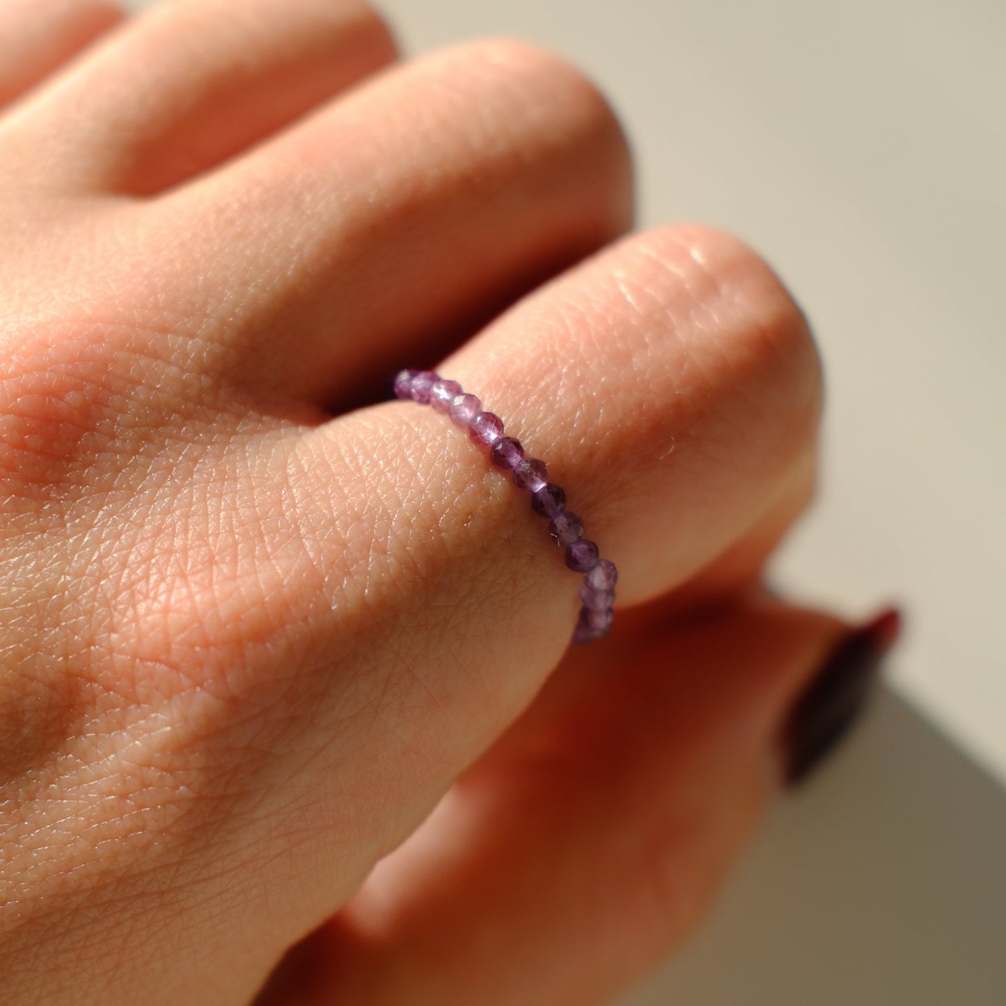 Hand wearing a purple beaded ring on a plain background