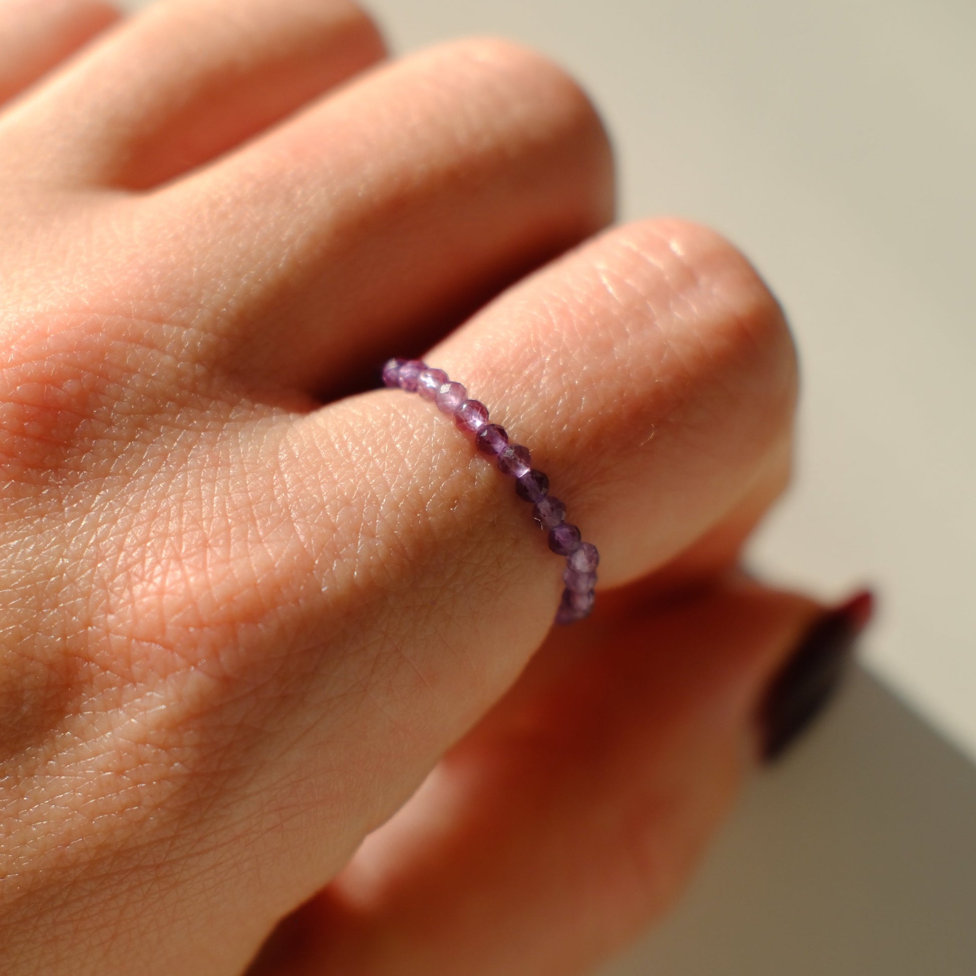 Hand wearing a purple beaded ring on a plain background