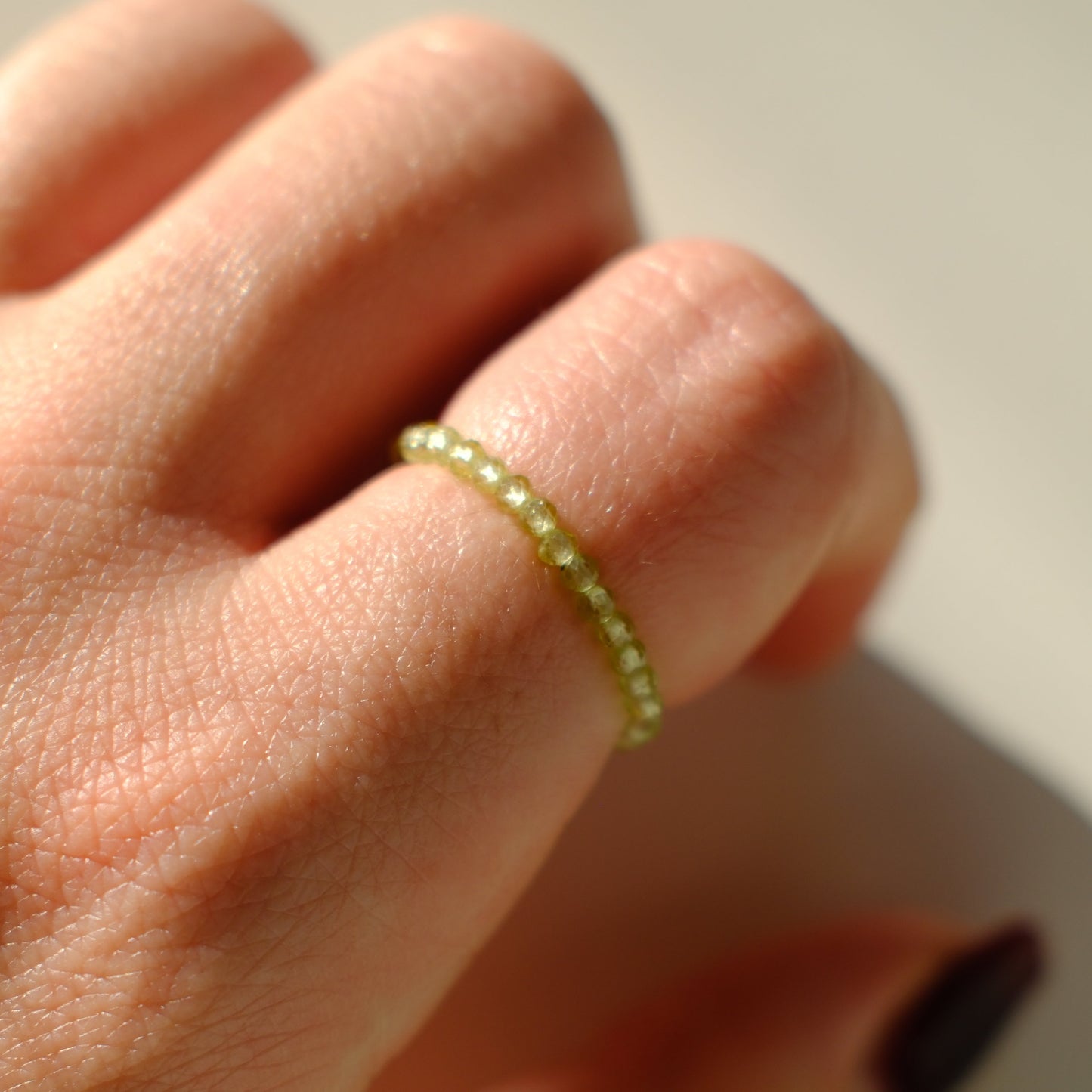 Close-up of a hand wearing a green beaded ring on a neutral background