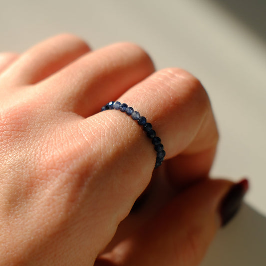 Close-up of a hand wearing a dark blue beaded ring on a neutral background