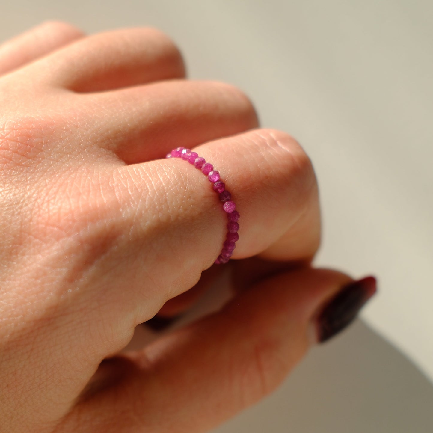 Hand wearing a pink beaded ring on a neutral background