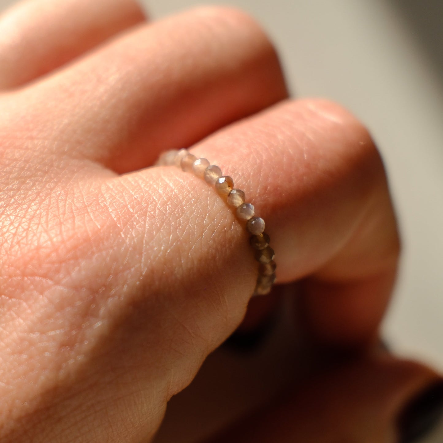 Close-up of a hand wearing a beaded ring on a neutral background