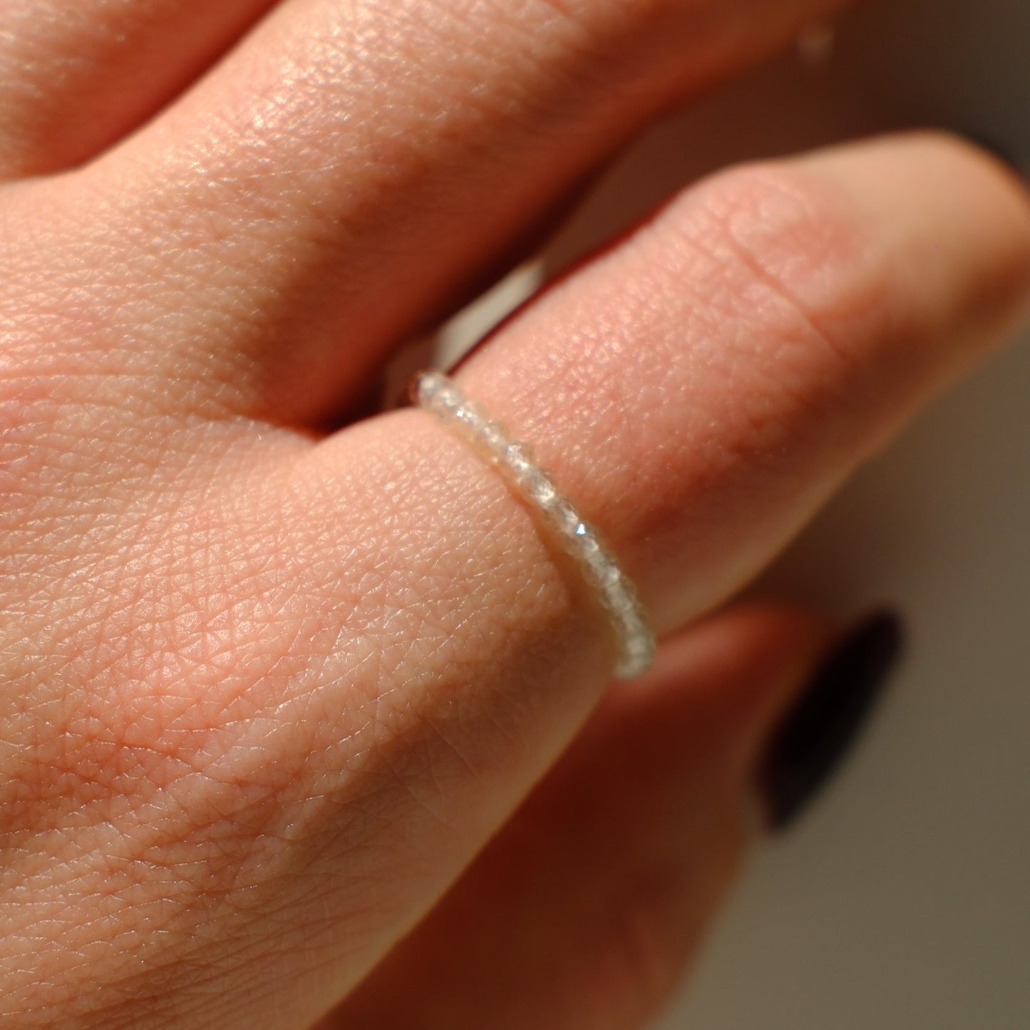 Close-up of a hand wearing a thin silver ring on a neutral background