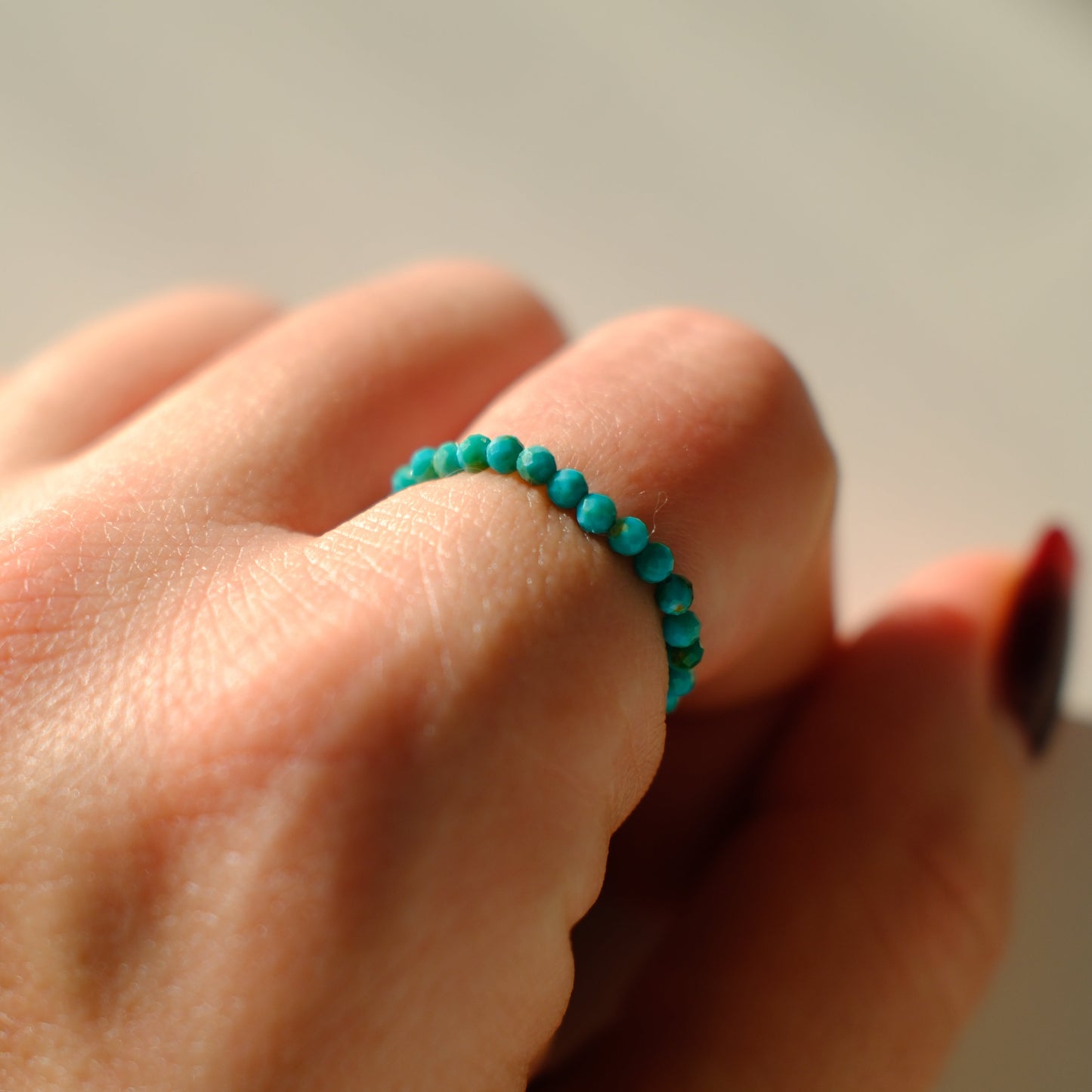 Turquoise beaded ring on a person's finger against a neutral background