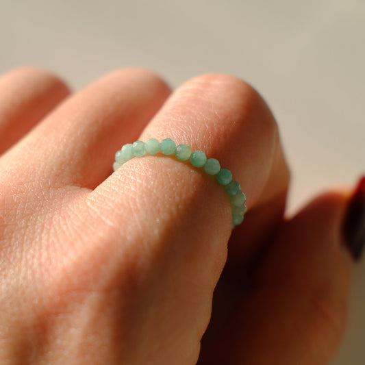 Close-up of a hand wearing a green beaded ring on a neutral background