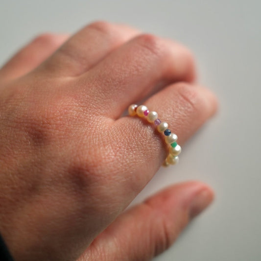 Close-up of a hand wearing a ring with multicolored beads on a neutral background