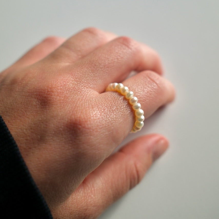 Hand wearing a pearl ring on a plain background