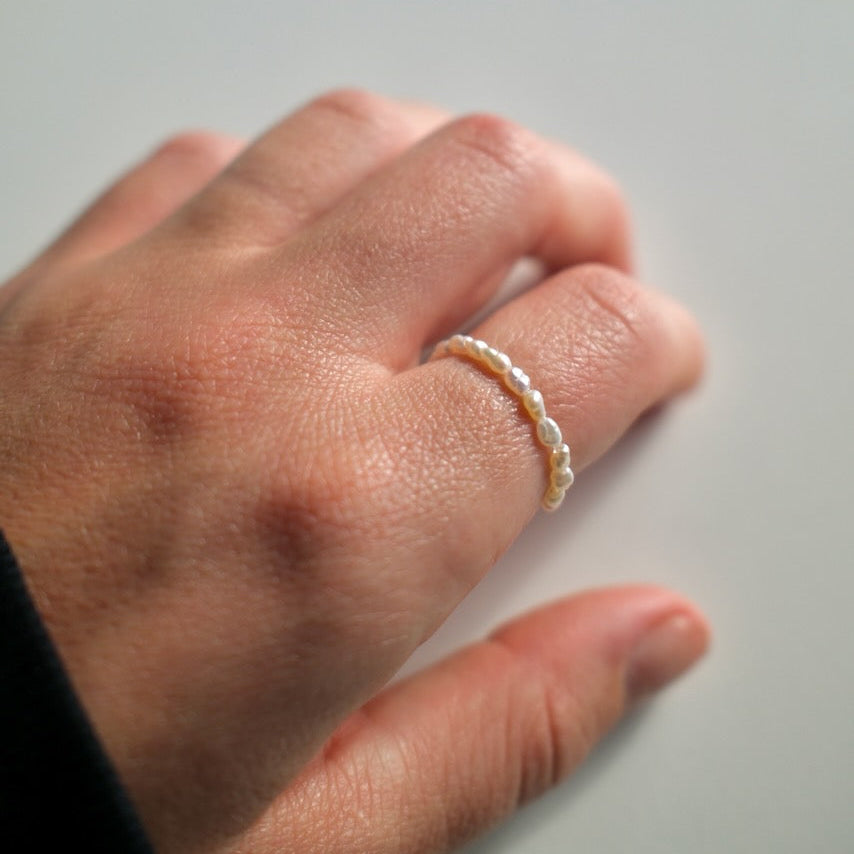 Hand wearing a pearl ring on a neutral background