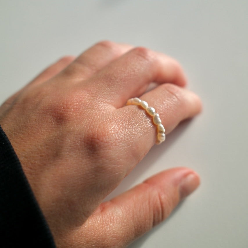 Hand wearing a pearl ring on a neutral background