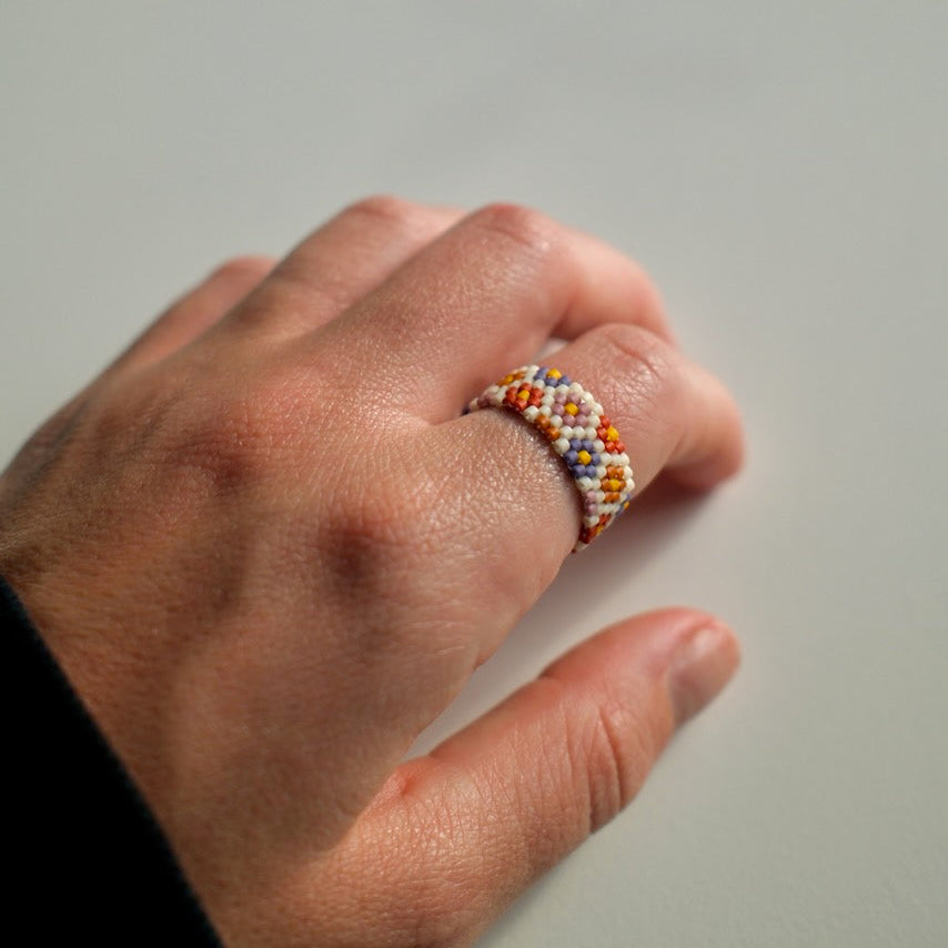 Hand wearing a colorful beaded ring on a plain background