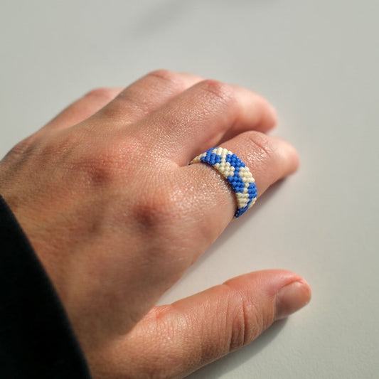 Hand wearing a blue and white beaded ring on a neutral background