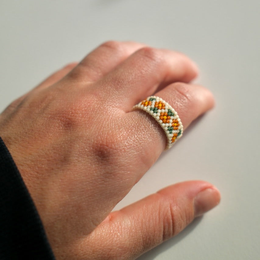 Hand wearing a beaded ring on a plain background