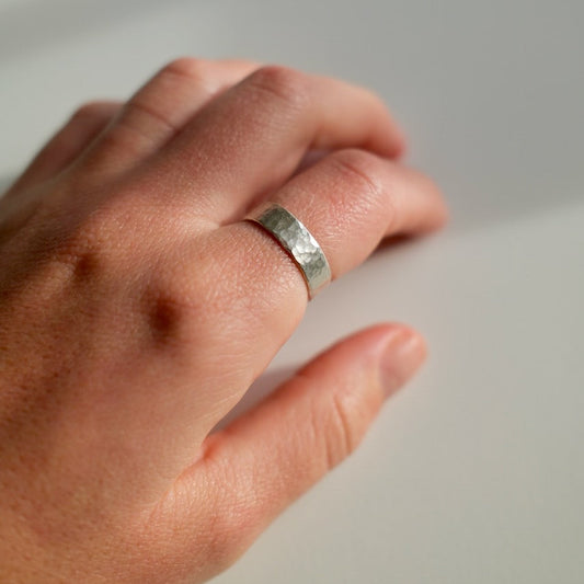 Hand wearing a silver ring on a neutral background