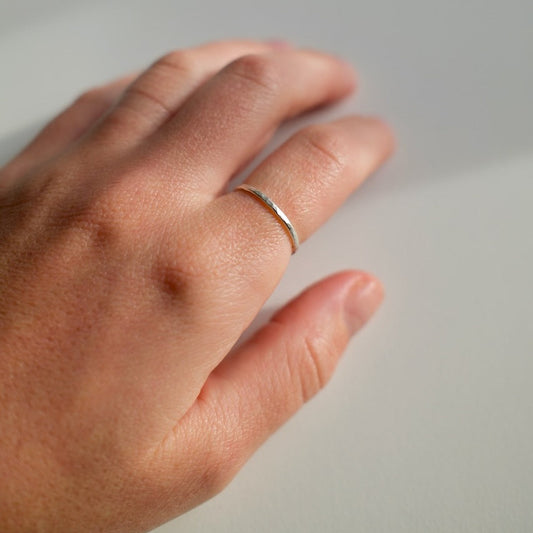 Hand wearing a thin silver ring on a neutral background